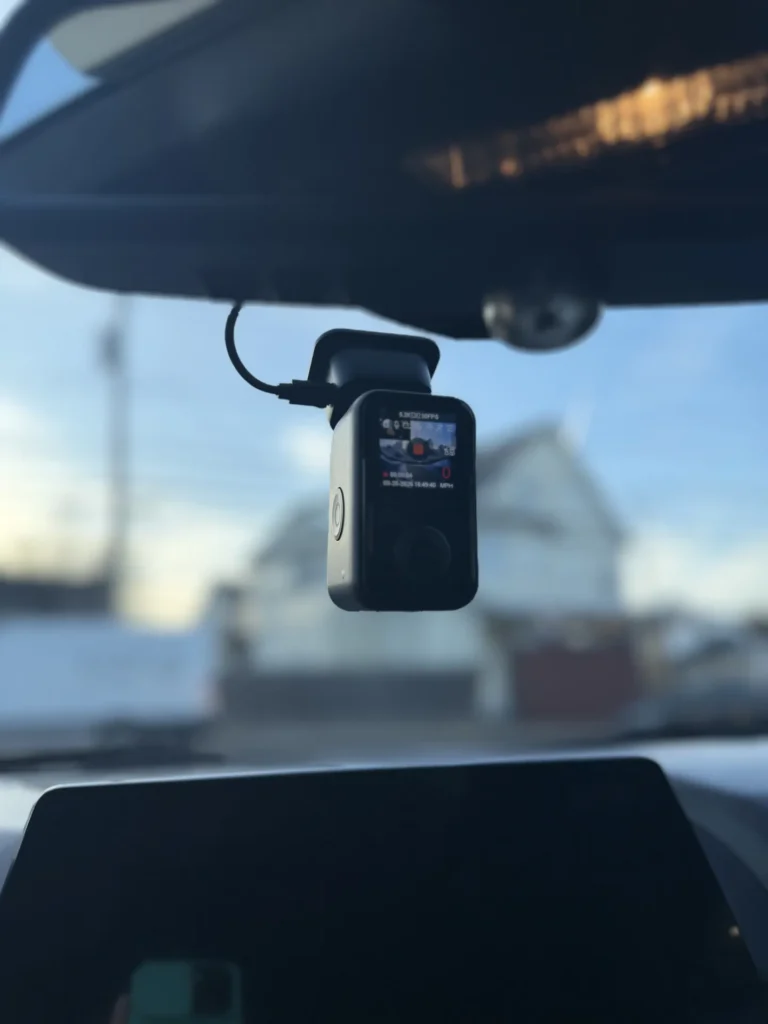 Dash cam installed behind the rearview mirror, its screen showing it's recording